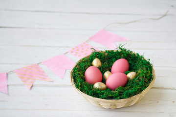 Easter. Pink and gold Easter eggs lie in a nest with moss on a white wooden background with a...
