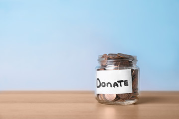 Glass jar with money and label DONATE on table against color background. Space for text