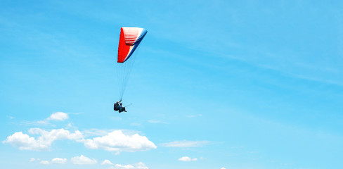 A colorful parachute with skydiver on a sunny blue sky background. Active lifestyle. Extreme sport. The concept of summer holidays, vacation, tourism. horizontal