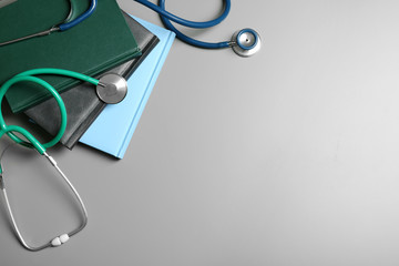 Student textbooks, stethoscopes and space for text on grey background, top view. Medical education