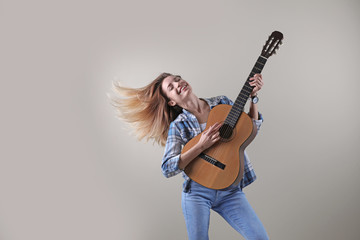 Obraz premium Young woman playing acoustic guitar on grey background. Space for text