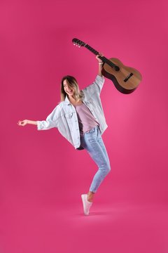 Young woman with acoustic guitar on color background