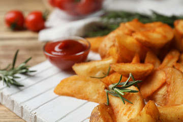 Wooden board with baked potatoes and rosemary on table, closeup