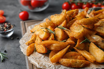 Wooden board with baked potatoes and rosemary on table, closeup