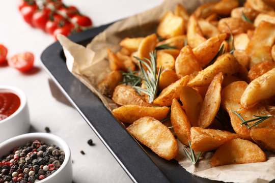 Baking sheet with potatoes and rosemary on table, closeup