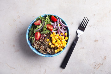 Healthy quinoa salad with vegetables in bowl and fork on color background, top view