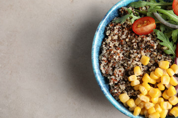 Healthy quinoa salad with vegetables in bowl on color background, top view. Space for text