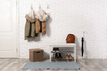 Stylish hallway interior with shoe rack and hanging clothes on brick wall