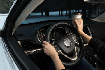 Obraz premium Young woman with coffee driving car along winter forest, closeup