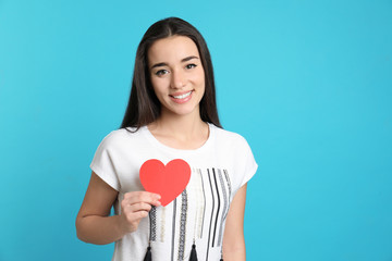 Portrait of beautiful young woman with paper heart on color background