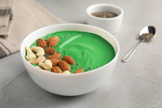 Bowl of spirulina smoothie with nuts and chia seeds on light table
