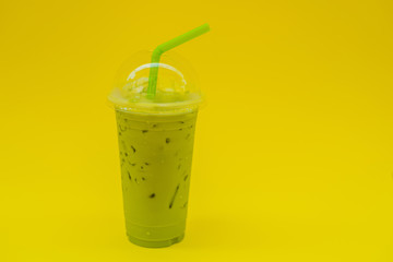Green tea latte with ice in plastic cup and straw in female hand with yellow manicure on yellow background. Homemade Iced Matcha Latte Tea with Milk take away