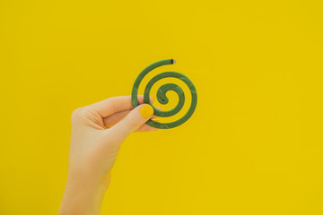 Burning mosquito coil is an anti-mosquito repellent on yellow background in hand with yellow manicure