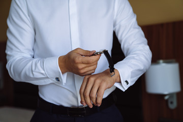 Close-up man puts on a gold watch with a leather belt, businessman is dressed in a stylish suit, a white shirt.