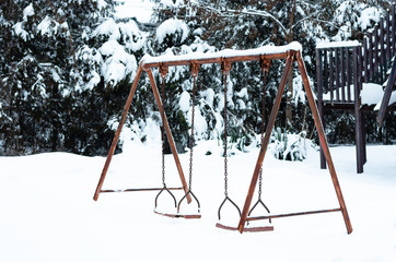 An old aged rusty  iron double swing  for children covered with snow in  park