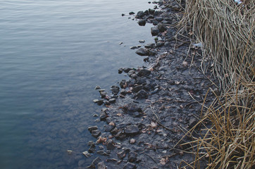 The dark rocky shoreline in the cool cold winter creek. 