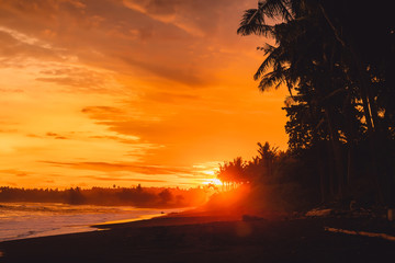 Bright sunset or sunrise with ocean waves and coconut palms in east coast of Bali