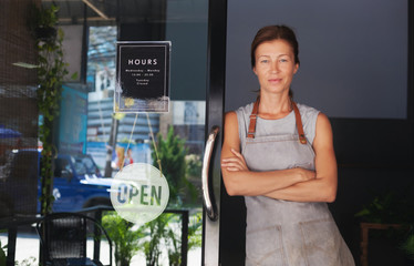 A female waitress in an apron, the owner of a cafe sits in the door of a cafe with a sign Open...
