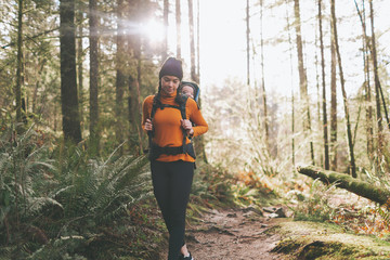 A young woman hiking through the forest with a baby on her back. 
