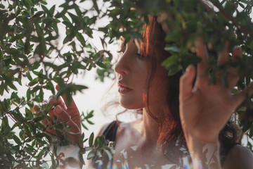 Portrait of a beautiful young woman with dark hair in a frame of branches and green leaves, summer and spring sensual portrait, natural beauty