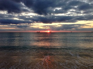 Sunrise on the Atlantic Ocean, South Beach, Miami, Florida, with seafaring container ships silhouetted in the distance against the rising sun