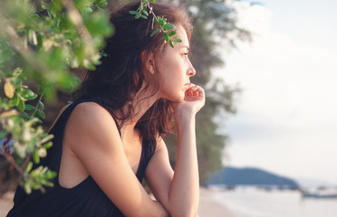 Portrait of a beautiful young woman with dark hair in a frame of branches and green leaves, on the...