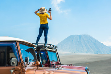Back view of woman standing on car and looking to Mount Batok volcano in Bromo tengger semeru national park, East Java, Indonesia. - obrazy, fototapety, plakaty