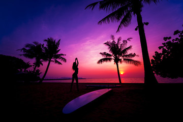 Silhouette of surfer girl with long surf board at sunset on tropical beach