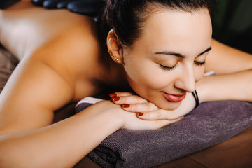Close up portrait of a amazing woman having body massage with hot stones therapy in spa salon. Young female relaxing spa resort .