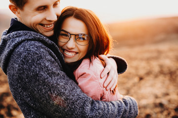 Lovely man hugging her woman laughing while traveling against sunset. Cute couple having fun together.