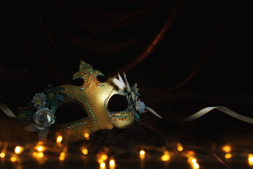 Photo of elegant and delicate gold venetian mask over dark velvet and silk background.