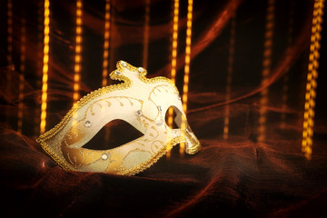 Photo of elegant and delicate gold, white venetian mask over dark velvet and silk background.