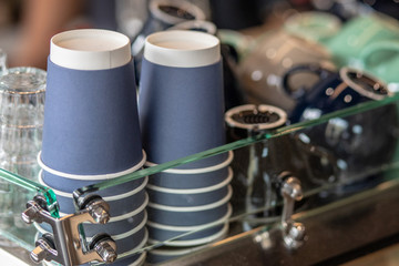 A stack of blue paper cups and coffee cups lies on the rack in a row. close up