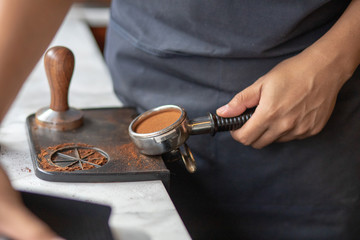 Barista using a tamper to press ground coffee into a portafilter. Close up photo