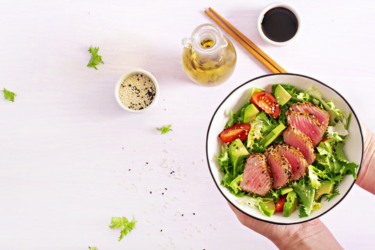 Japanese traditional salad with pieces of medium-rare grilled Ahi tuna and sesame with fresh vegetable salad on a plate. Plate with salad in hands. Authentic Japanese food. Top view. Copy space.