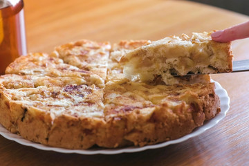 Close-up woman's hands takes a slice of a homemade apple pie from plate. Teapot on the table.