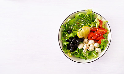 Fototapeta na wymiar Fresh salad with avocado, tomato, olives and mozzarella in a bowl. Buddha bowl. Fitness food. Vegetarian meal. Top view