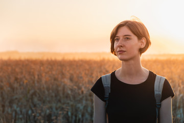 Backlit portrait of a woman in sunset. Female person standing in evening sunlight at a field