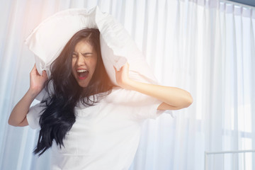 Young woman lying in bed suffering from sound covering head and ears with pillow making unpleasant face.Do not oversleep again