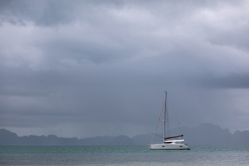 white yacht with sail set goes along the island on cloudy day. cloudy sky.