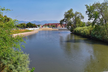 Views of Jordan River Trail with surrounding trees, Russian Olive, cottonwood and silt filled muddy water along the Wasatch Front Rocky Mountains, in Salt Lake City, Utah.