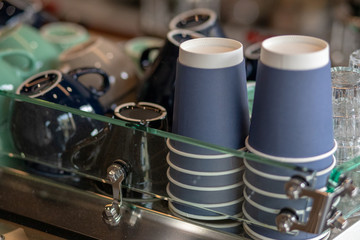 A stack of blue paper cups and coffee cups lies on the rack in a row. close up