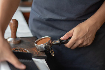 Barista using a tamper to press ground coffee into a portafilter. Close up photo