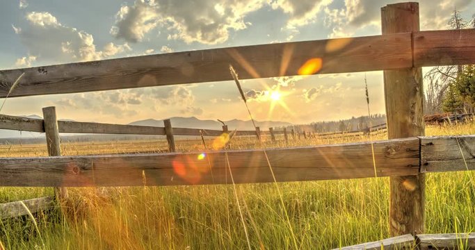 The sun sets over the Sawtooth Mountains in Idaho, framed by a wooden farm fence. HDR Time lapse.