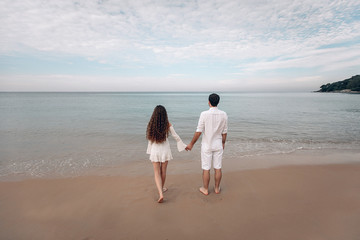 Young Couple looking at the sea and overcast sky in white clothing. Back view. Phuket. Thailand. Trip to warm destination.