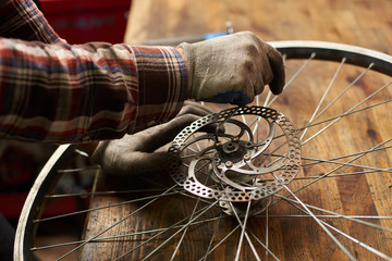 Cropped view of male mechanic working in bicycle repair shop, serviceman repairing bike wheel using...