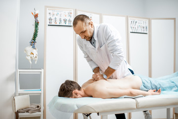 Professional senior physiotherapist doing manual treatment to a men's thoracic spine in the cabinet of rehabilitation clinic - obrazy, fototapety, plakaty