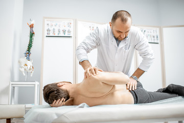 Obraz na płótnie Canvas Professional senior physiotherapist doing manual treatment to a man in the cabinet of rehabilitation clinic