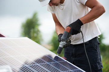 Technician worker assembling shiny solar photo voltaic panels using electrical screwdriver standing...