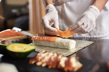 Closeup view of process of preparing rolling sushi with disposable gloves on bamboo mat